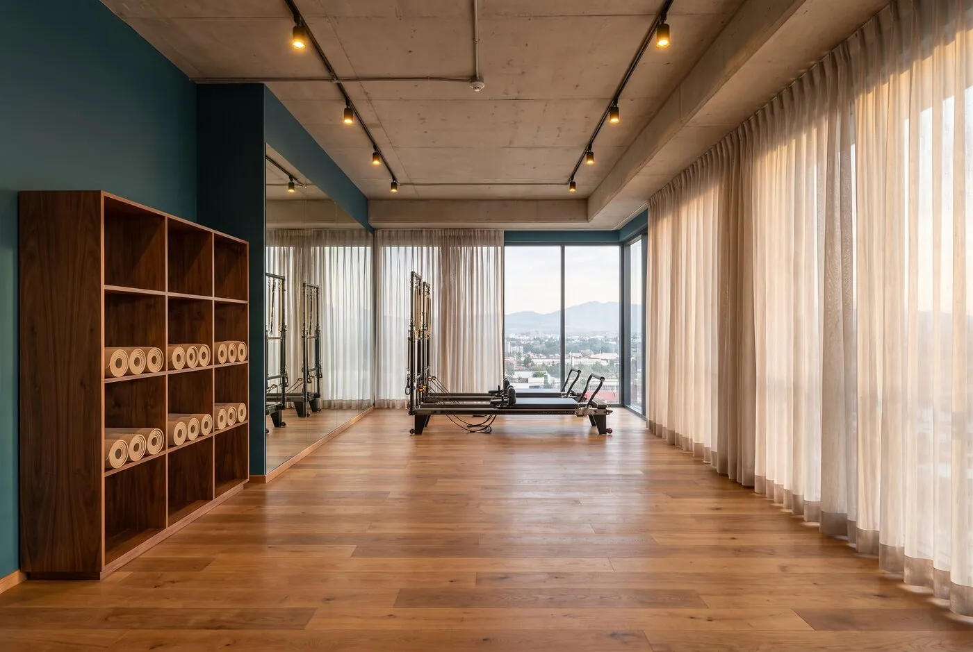 Estudio de yoga y pilates con piso de madera, reformers y cortinas traslúcidas